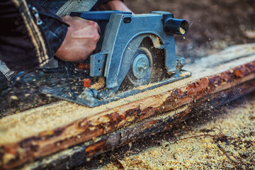 Circular saw for cutting boards into the hands of the builder, the man sawed bars, construction and home renovation, repair and construction tool. Carpenter Using Circular Saw for wood. Close-up