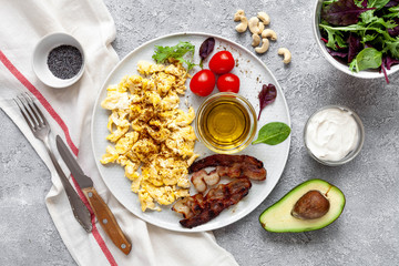 Fototapeta na wymiar Keto breakfast with scramble eggs, avocado, tomatoes, cream and bacon
