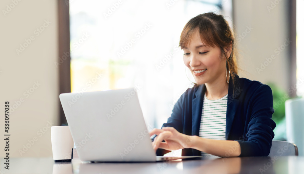 Wall mural happy young businesswoman using laptop computer doing online shopping at cafe. smiling beautiful asi