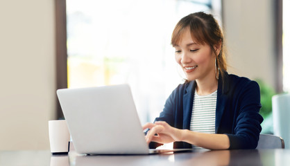 Happy young businesswoman using laptop computer doing online shopping at cafe. Smiling beautiful Asian woman sitting and working at her workplace. Lifestyle, Technology, Internet