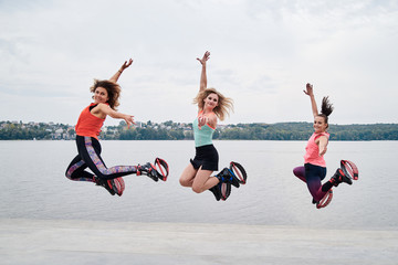 A group of young fit slim women in kangoo jumps, jumping in the air in front of city lake in...