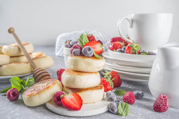 Cottage cheese pancakes with honey and various summer berry on grey background, summer breakfast or lunch