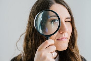 on a gray background young girl looking through a magnifying glass
