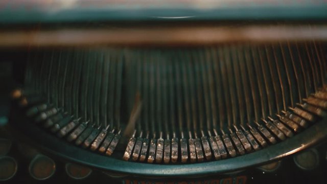 Cinematic dolly shot across typewriter strikers moving on old typewriter. Camera moves right to left as the keys type.