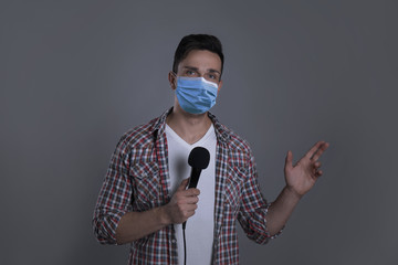 Young journalist with microphone wearing medical mask on grey background. Virus protection