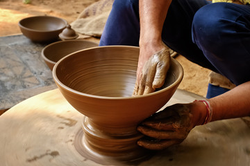 Fototapeta na wymiar Pottery - skilled wet hands of potter shaping the clay on potter wheel. Pot, vase throwing. Manufacturing traditional handicraft Indian bowl, jar, pot, jug. Shilpagram, Udaipur, Rajasthan, India