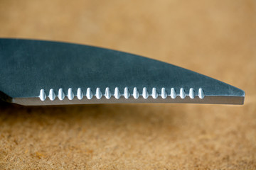 One blade with notches from scissors for cutting fish and meat on the wooden background close up
