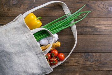 Woven bag of different health food on dark wooden table background. Green onion, garlic, tomato and...