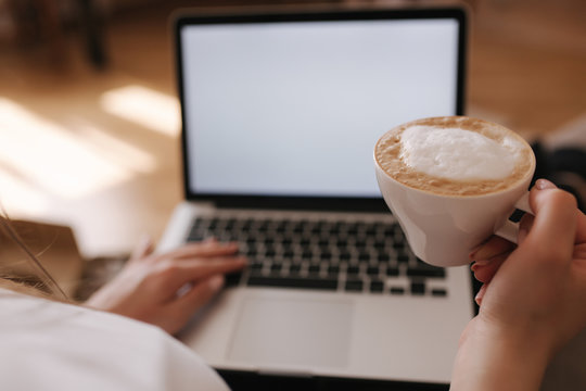 First Person View Of Female Working At Home. Woman Work On Laptop And Drink Cappuccino. Mock Up, White Screen. Quarantine Time