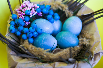Fototapeta na wymiar Easter holiday, background and decor of painted blue eggs in nest of flowers, branches. Religion and traditions.