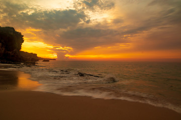 Seascape. Sunset time. Sunlight reflection. Beach with rocks. Ocean with motion blur waves. Slow shutter speed. Tegal Wangi beach, Bali, Indonesia