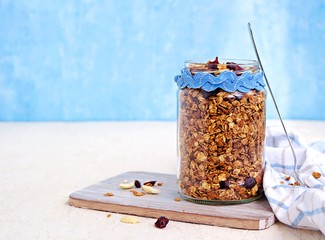 Homemade baked oat granola with nuts, dried cranberries and honey in a glass jar on a light...