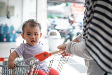 happy infant baby sitting alone in shopping cart or trolley in grocery supermarket