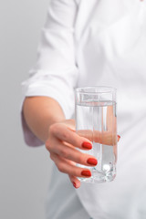 Glass of water in female hand of doctor on white background close up.
