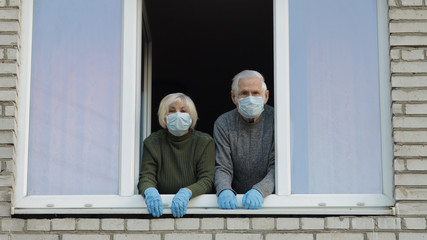 Old grandparents stay at window isolated at home on quarantine. Coronavirus