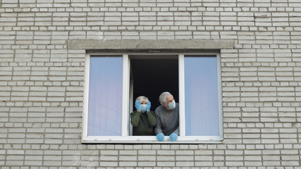 Fototapeta na wymiar Old grandparents stay at window isolated at home on quarantine. Coronavirus