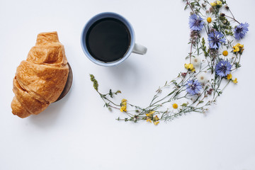 Fototapeta na wymiar Cup of coffee and croissant with wildflowers