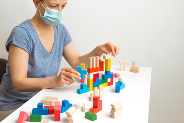 A woman in a medical mask plays dice at home. Quarantine concept.