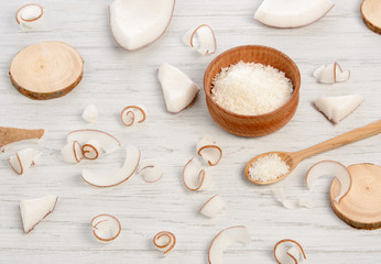 Coconut pulp slices and spiral curls with wooden spoon, bowl and circles on white table
