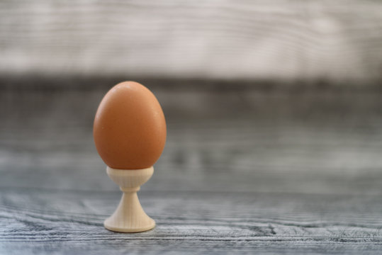 One egg standing in holder on the wooden background.