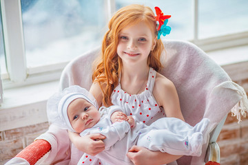 Charming pretty girl teenager holds in her arms her younger newborn sister. Older sister holding body of her little sibling. Concept of Siblings friendly in children. Baby care concept