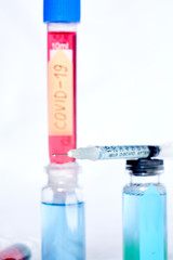 A syringe for injection with a coronavirus vaccine, antiviral tablets and 2 syringes with red and yellow liquids on a white background