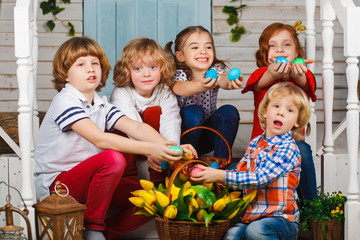 Children holding easter eggs. Beautiful children sit near the basket with tulips and hold Easter eggs in their hands. Funny moments