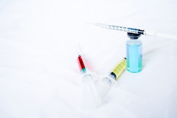 A syringe for injection with a coronavirus vaccine, antiviral tablets and 2 syringes with red and yellow liquids on a white background