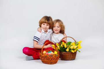 Fototapeta na wymiar Two little boys are sitting with a basket of Easter eggs and a basket of tulips. White background. Funny moments
