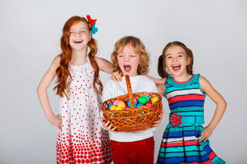Three beautiful children are standing with a basket of Easter eggs. Funny moments. White background.  Spring holidays concept. Family Easter celebration.