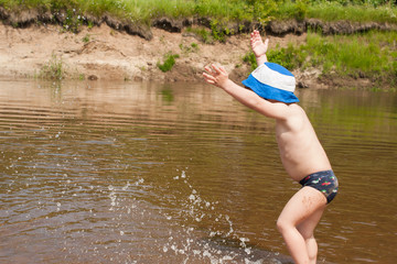 Cute baby boy splashes on the riverbank