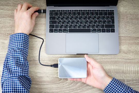 Man Is Connecting A Portable Hard Drive To The Laptop For Data Transfer Or Backup