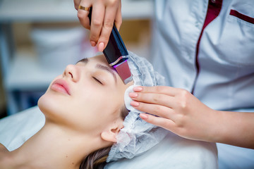 Woman receiving ultrasonic facial exfoliation at cosmetology salon. Procedure clearing clogged...