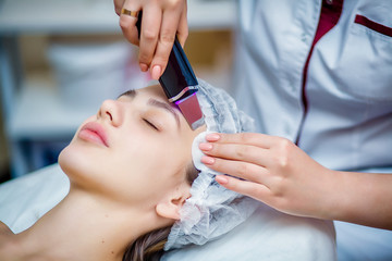 Woman receiving ultrasonic facial exfoliation at cosmetology salon. Procedure clearing clogged pores, ultrasonic treatment for skin rejuvenation, beautician uses modern apparatus for refreshing