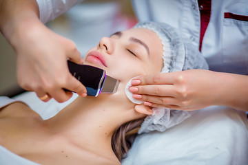 Woman receiving ultrasonic facial exfoliation at cosmetology salon. Procedure clearing clogged...