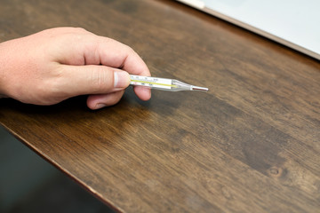 Closeup of medical thermometer in hand on wooden table