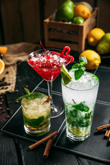 Fresh sweet alcohol cocktails in different glasses, mojito cosmopolitan and mai tai on the dark wooden background, closeup, vertical