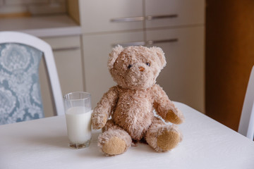 A glass of milk and Teddy bear on the kitchen table.Positive morning for children. Delicious, healthy drink.