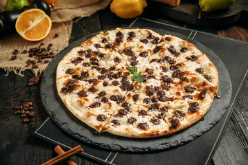 Side view on delicious sweet pizza dessert with chocolate chips on the black board on the black wooden table, horizontal
