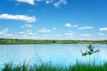 The blue sky with the clouds above the clear blue lake. Summer landscape