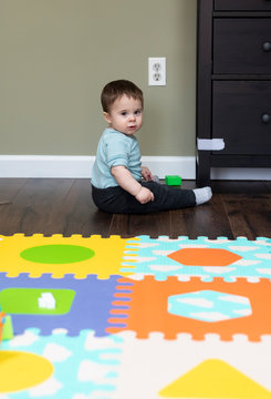 Baby boy sitting near baby proofed electrical outlets and drawers