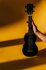 Classic black ukulele guitar in the hand on yellow wall