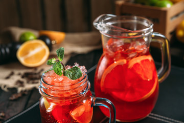 Closeup on fresh red orange sweet lemonade in jars on the dark wooden background, horizontal, side view