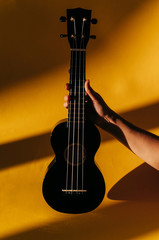 Classic black ukulele guitar in the hand on yellow wall