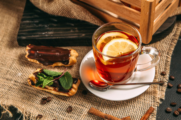 Hot and healthy black tea with lemon in a mug with eclair, wooden table, leaves, horizontal, side view
