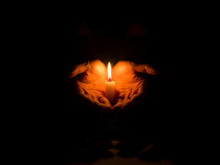 two hand holding a burning candle in dark