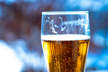 Light beer in a glass goblet on a picnic with snow background. Beer foam on the walls of a glass in the sunlight