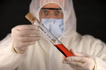 The doctor in a protective suit and mask holding a glass tube with a positive blood test result for...