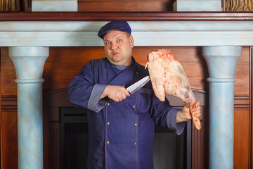 Half legth shot of thoughtful male chef, holds very big red raw piece of meat, needs to chop for...