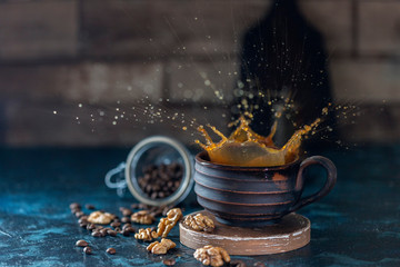 Splash of iced coffee in handmade ceramic mug and roasted beans and nuts on a dark background.